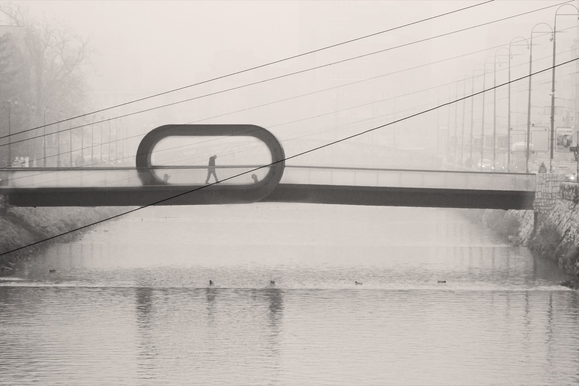 A figure crossing the Festina Lente bridge in fog, the span loops back on itself mid-crossing.